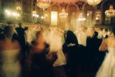 a blurry photo of people dancing at a wedding in an ornate building with chandeliers