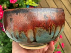 a hand holding a brown and blue bowl in front of some pink flowered plants