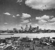 black and white photograph of city skyline with water in foreground, clouds in the sky