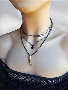 A black steel and 24 K gold filled steel Gothic Grunge alt aesthetic choker chain layered necklace set with heart and tusk pendants. The set is two separate necklaces that can be worn together or separate, one is a black steel horse eye paperclip chain choker with a built-in extender that runs from approximately 14" to 16". it also features a two strand necklace, one black steel with a gold filled tusk pendants and the other 24 K gold filled steel chain with a black heart charm. It is an adjustable length from approximately 16" to 18" with a built-in extender.  This necklace set is an excellent handmade gift for someone special. It is a perfect choice for those who love alternative and goth styles, as well as anyone who wants to make a statement with their jewelry. Punk Gold Stainless Steel Jewelry, Edgy Black Necklaces For Gift, Edgy Black Necklaces For Gifts, Edgy Black Necklace For Gift, Edgy Black Necklace As Gift, Black Grunge Necklace For Gift, Black Metal Clavicle Chain Charm Necklace, Black Grunge Necklace With Adjustable Chain, Edgy Black Chain Necklace For Gifts