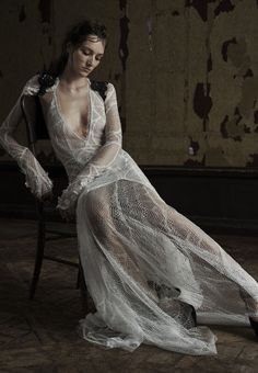 a woman is sitting on a chair wearing a white dress with sheer fabric and high heels