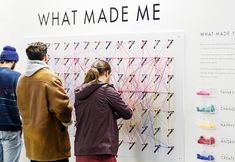 three people standing in front of a wall that has an art piece on it and the words what made me written on it