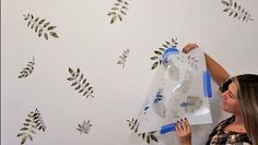 a woman is painting a wall with stencils on it and leaves are painted on the wall behind her