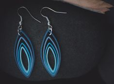 a pair of blue earrings sitting on top of a black stone surface next to a piece of wood