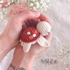 a person holding a small crocheted animal with flowers on it's head