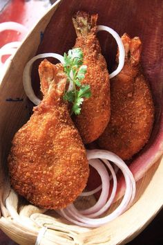 two pieces of fried chicken in a wooden bowl with onions and parsley on the side