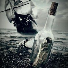 an empty bottle sitting on top of a beach next to a ship in the ocean