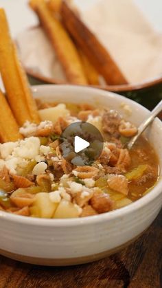 a white bowl filled with soup next to some french fries on top of a wooden table