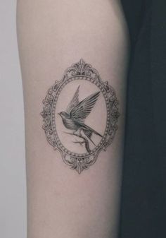 a small bird tattoo on the right arm, with an ornate frame around it's neck