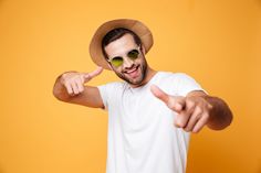 a man wearing sunglasses and a hat pointing at the camera with his thumb up on an orange background