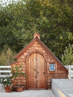 a small wooden building with a potted plant next to it and a white fence in the background