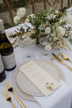 the table is set with wine, silverware and flowers