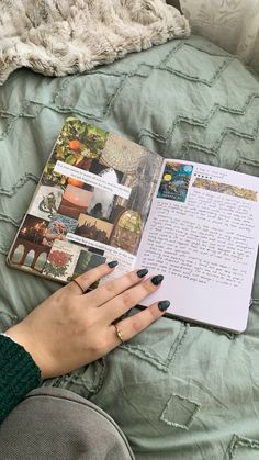 a woman's hand holding an open book on top of a green quilted bed