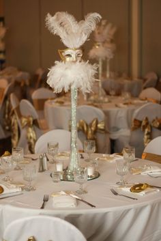 the centerpieces are decorated with white feathers and gold rimmed glasses, along with silverware