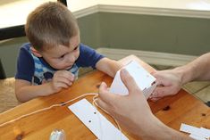 a young boy sitting at a table with an adult holding a nintendo wii game controller