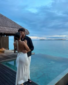 a man and woman standing next to each other in front of a pool at dusk