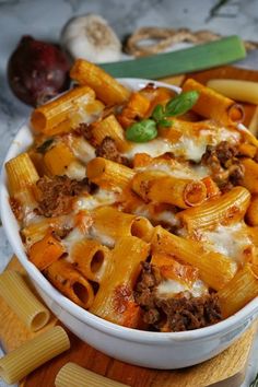 a white bowl filled with pasta and meat on top of a wooden cutting board next to vegetables