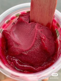 a hand holding a plastic container filled with red colored food and a wooden spatula