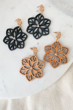 three pairs of wooden earrings on a white marble surface with black and gold details in the shape of flowers