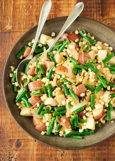 a bowl filled with green beans, ham and other food on top of a wooden table