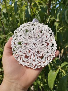 a hand holding a white paper doily in front of some trees