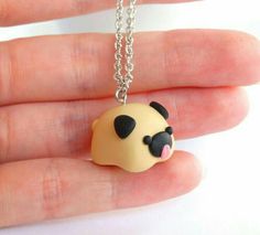 a hand holding a tiny necklace with a small dog on it's face and tongue sticking out