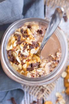 a glass jar filled with chocolate and nuts on top of a blue towel next to a spoon