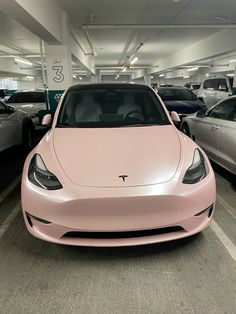 a pink tesla car parked in a parking garage next to other cars on the street