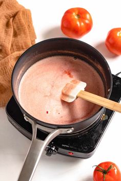 a pan filled with food sitting on top of a stove next to tomatoes and a wooden spoon