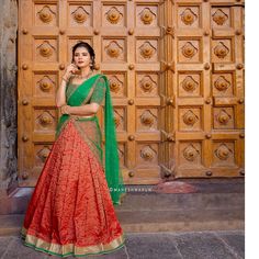 a woman standing in front of a wooden door wearing a red and green lehenga