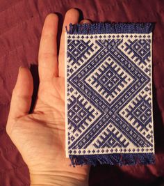 a hand is holding a small piece of cloth with blue and white designs on it