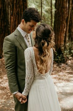 a bride and groom holding hands in the woods with their back turned to look at each other