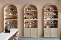 three wooden shelves with bottles on them in front of a white counter top and chairs