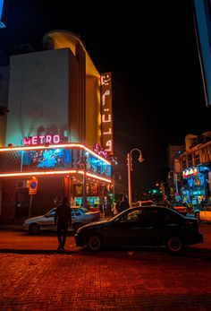 a car parked on the side of a road next to a tall building with neon lights