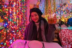 a woman sitting at a table with a plate and glass in front of colorful lights