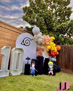 an outdoor birthday party with balloons and anime characters on the lawn, in front of a fence