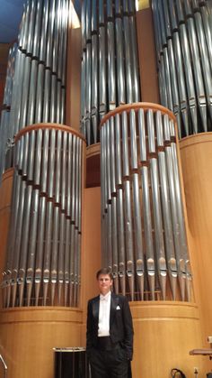 a man in a suit and tie standing next to a large pipe organ that has been built into the wall