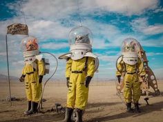 three people in yellow spacesuits standing next to each other on a desert plain