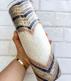 a hand holding a coffee cup with gold, blue and white designs on the outside