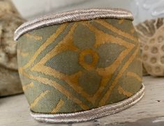 Hand made Fortuny fabric wide Cuff Bracelet IMPERO No. 5077  in Yellow and Silvery Gold  long staple cotton  An upscale hand made one of a kind hefty  Fortuny Cuff Bracelet  This can be a formal looking piece and would be lovely for a wedding, prom or special event yet travels easily anywhere and looks great with jeans and a T Shirt.  IMPERO is a classic Fortuny damask featuring blossoms and blooms The fabric used for this bracelet was taken from a vintage set of draperies. The colors have aged beautifully which is much desired by collectors. The gold metallic dye has turned a mellow bronze.  Features a glistening double band of carefully preserved new old stock Antique Silver Metallic cord trim from a now closed NY garment district shop.  Lined with the most luxurious stain resistant soft Fortuny Fabric, Luxury Gifts For Her, 2024 Style, Wide Cuff Bracelets, Bronze Gold, Wide Cuff, Beautiful Hats, Fashion Fall, Silk Velvet