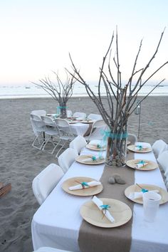 a table set up on the beach with plates and place settings for people to eat