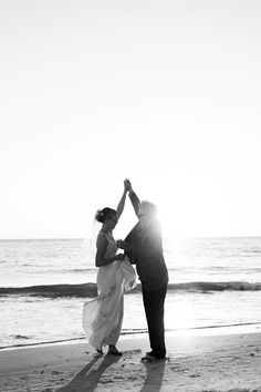 a bride and groom are standing on the beach holding their hands up to each other