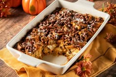 a casserole dish with pecans and pumpkins in the background on a table