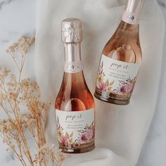 two bottles of rose wine sitting on top of a white cloth next to dried flowers