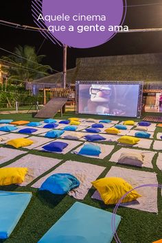 an outdoor movie screen with blue and yellow blankets on the ground in front of it