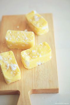 four pieces of yellow cake sitting on top of a wooden cutting board