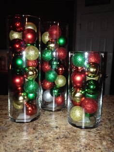 three glass vases filled with ornaments on top of a counter