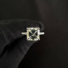 an engagement ring with a square cut diamond in the center on a black cloth background