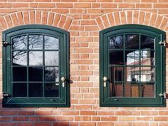 two windows on the side of a brick building with green shutters and wood trim