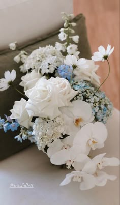 a bouquet of white and blue flowers sitting on top of a table next to a pillow